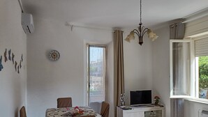 Un comedor con una mesa preparada para cuatro personas, un televisor en un mueble y una ventana con cortinas.