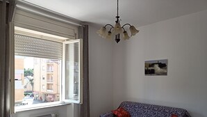 Una habitación con sofá, radiador, ventana con persianas, lámpara colgante y un pequeño cuadro en la pared.
