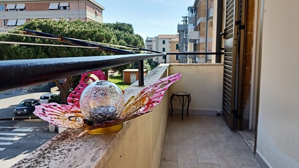 Un balcón con una esfera de cristal decorativa y una mariposa, una pequeña mesa, y vistas a la calle y edificios.