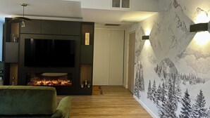 Un salon moderne avec un téléviseur à écran plat, une cheminée et un fauteuil vert confortable.