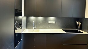 Une cuisine moderne avec des meubles de couleur sombre, un dosseret en marbre et un évier en acier inoxydable.