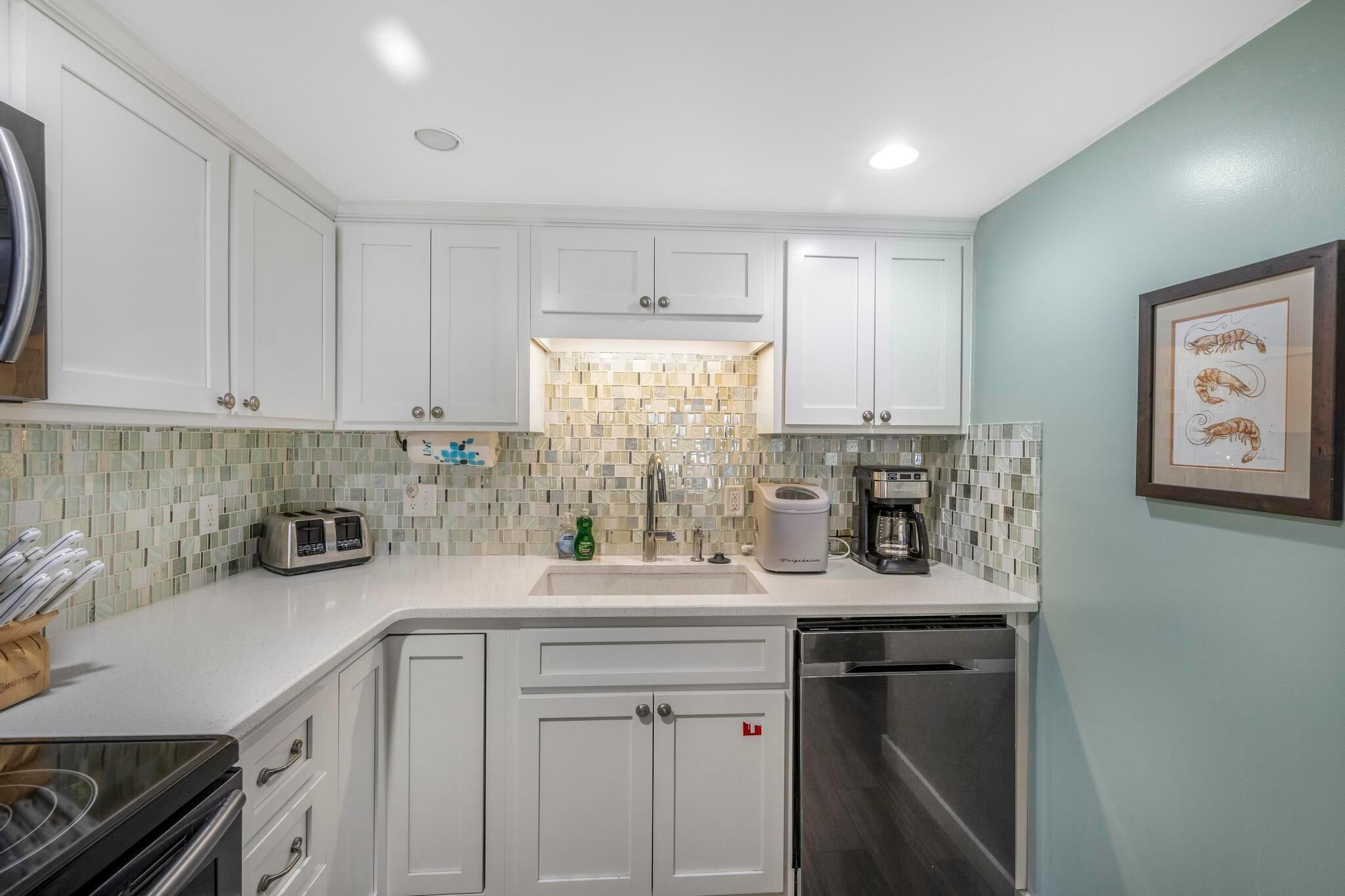 A modern kitchen with white cabinets, a tiled backsplash, a coffee maker, and a dishwasher.