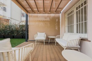 A covered patio with white furniture, including chairs and a sofa, and a window with white shutters. - BOUTIQUE HOME  (L'Hospitalet de Llobregat)