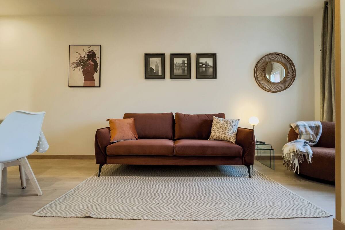 A living room with a brown sofa, a white chair, and a patterned rug.