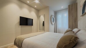 Una camera da letto con un letto, una TV a schermo piatto montata a parete, una ventola a soffitto e una finestra con tende.