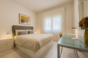 A bedroom with a bed, bedside tables, a glass table, a lamp, a vase with flowers, and a window with curtains. - BOUTIQUE HOME  (L'Hospitalet de Llobregat)
