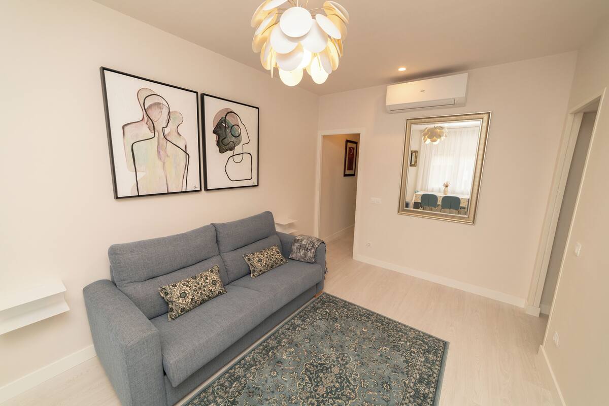 A modern living room with a grey sofa, patterned rug, and abstract wall art.