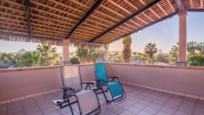 A covered balcony with two lounge chairs and a small table, overlooking a landscape with palm trees and distant mountains. - 7bdrm  boutique hotel with AC, WiFi , heated pool convenient location. (Loreto)