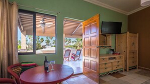 A room with a wooden table, chairs, a TV on the wall, and a view of palm trees outside. - 7bdrm  boutique hotel with AC, WiFi , heated pool convenient location. (Loreto)