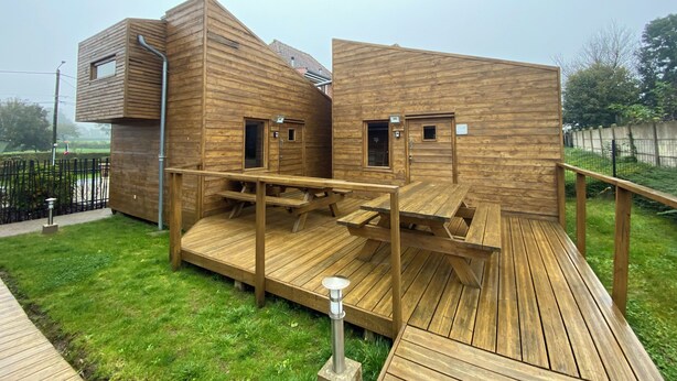 Eine Holzhütte mit einer Veranda und einem kleinen Anbau, mit Tür und Fenstern.