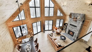 A spacious loft-style living area with large windows, a fireplace, and a high ceiling. - Magnificent ski-in/out wooden chalet in Mont-Blanc with SPA and billiard table! (Mont-Blanc)