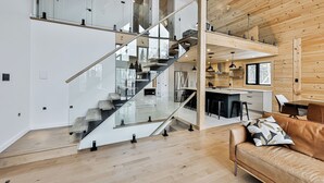A modern interior with a staircase leading to a loft area, a kitchen with bar seating, and a leather sofa. - Magnificent ski-in/out wooden chalet in Mont-Blanc with SPA and billiard table! (Mont-Blanc)