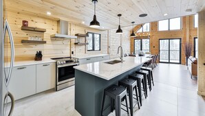 A modern kitchen with a central island, bar stools, and a large window providing natural light. - Magnificent ski-in/out wooden chalet in Mont-Blanc with SPA and billiard table! (Mont-Blanc)