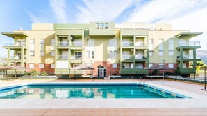 Ein modernes Apartmenthaus mit Schwimmbad, Balkonen und blauem Himmel.
