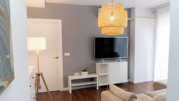 Ein modernes Wohnzimmer mit Fernseher, einem weißen Lowboard, einer Stehlampe und einem beigen Sofa.
