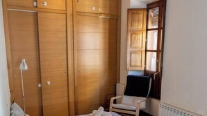 A cozy living room with a dark sofa, a chair, and a wooden wardrobe. - Puerta Real Apartments (Granada)