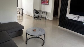 Una sala de estar moderna con un sofá gris, una mesita redonda pequeña, un televisor y un cuadro en la pared.