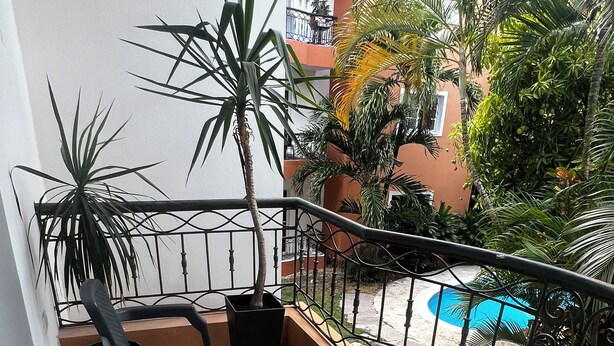 Un balcón con dos sillas negras, una mesa blanca y una planta en maceta.
