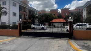 Zona residencial cerrada con varios edificios, una entrada vigilada y coches estacionados.