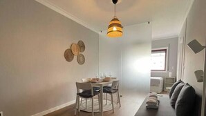 A modern living room with a dark sofa, a dining area with a round table and chairs, and a hanging light fixture. - Nice apartment in Gaia next to Bodegas (Vila Nova de Gaia)
