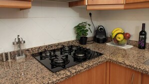 A kitchen with granite countertops, a gas stove, wooden cabinets, a potted plant, a fruit bowl, a coffee maker, and a bottle of wine. - To complete (Granada)