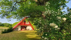 Een huis met een rood dak en een klein terras, omringd door weelderige begroeiing en witte bloemen.