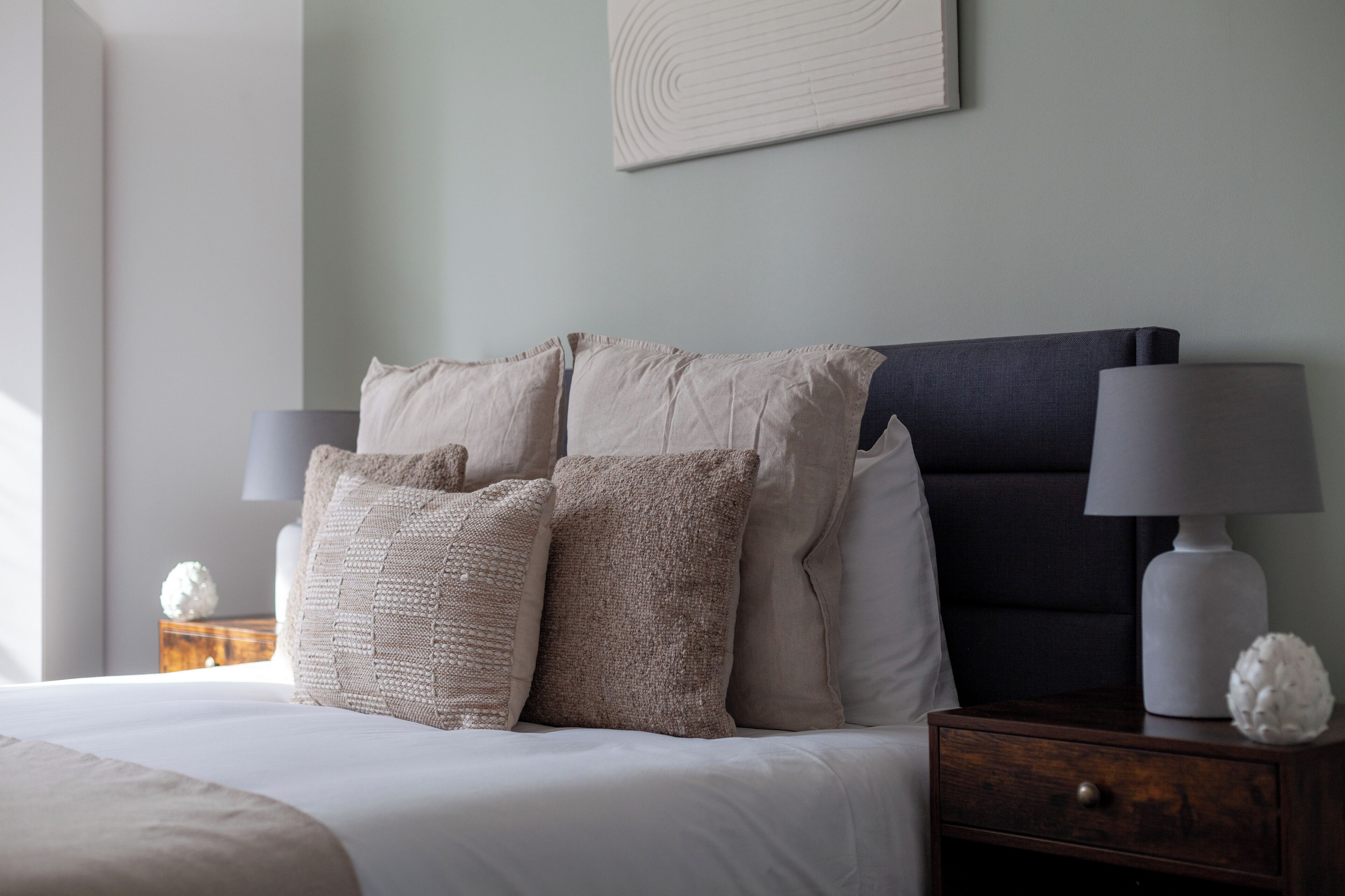 A neatly made bed with multiple pillows, a dark headboard, and bedside lamps.