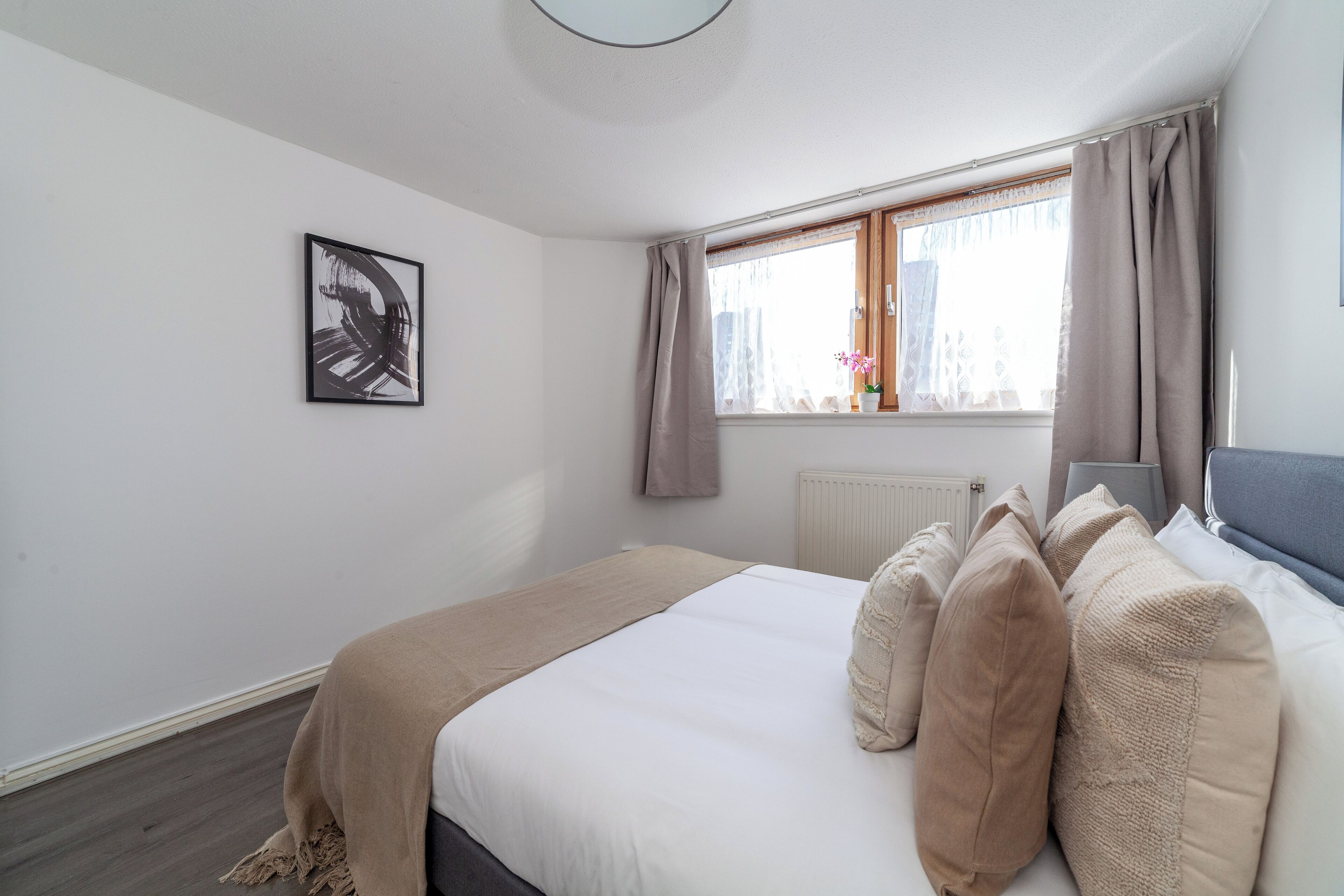 A bedroom with a large bed, a window with curtains, a radiator, and a framed picture on the wall.