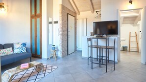 Una sala de estar moderna con un sofá, una mesa de centro y un televisor. Cuenta con una zona de cocina con mostrador y taburetes.