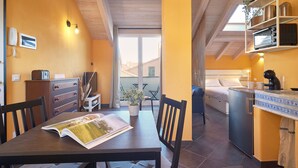 Una habitación compacta con mesa de comedor, sillas, una pequeña kitchenette, cama y balcón con vistas.