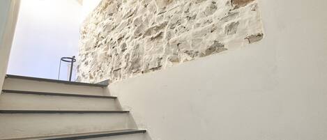 Una escalera que sube hacia un muro de piedra con un tragaluz circular.