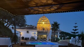 Un patio al aire libre con piscina, muebles de mimbre y un colgante decorativo.