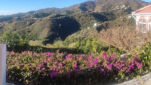 Paisaje montañoso con campos en terrazas y un edificio de techo rojo.