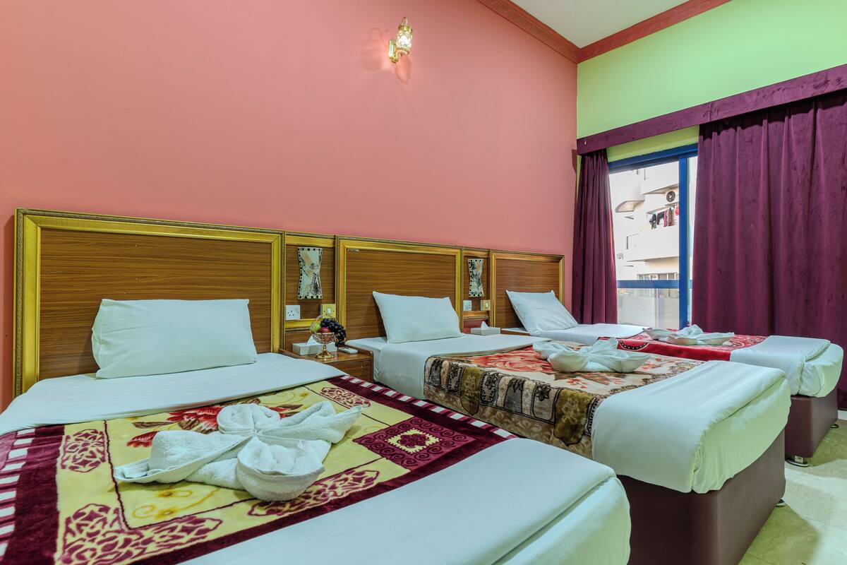 A hotel room with three beds, each with white linens and decorative headboards.