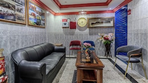 A lobby with a black leather sofa, a wooden coffee table, and two chairs. There is a clock on the wall and a framed picture above the sofa. - City Relax Hotel (Dubai)