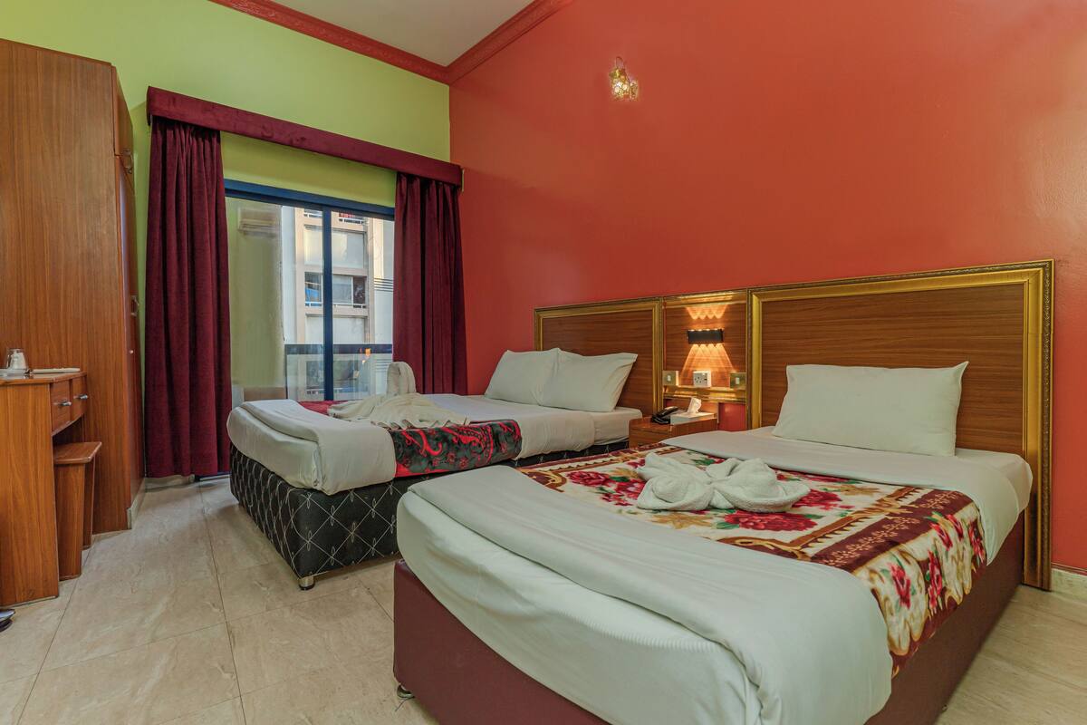A hotel room with two beds, a wooden wardrobe, a desk, and a window with curtains.