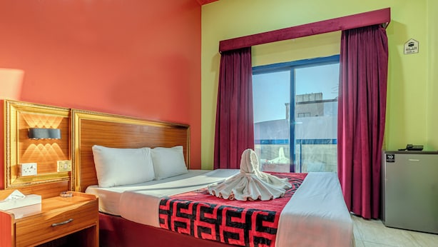 A hotel room with a bed, a nightstand, a lamp, a refrigerator, and a window with curtains. - City Relax Hotel (Dubai)