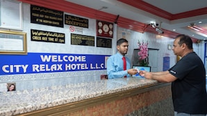 A hotel reception desk with a "Welcome City Relax Hotel L.L.C." sign, a clock, and a "No Smoking" sign. - City Relax Hotel (Dubai)