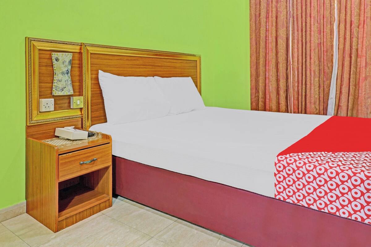 A bed with white bedding, a wooden nightstand with a drawer, a bedside table, and a red and white patterned bedspread.