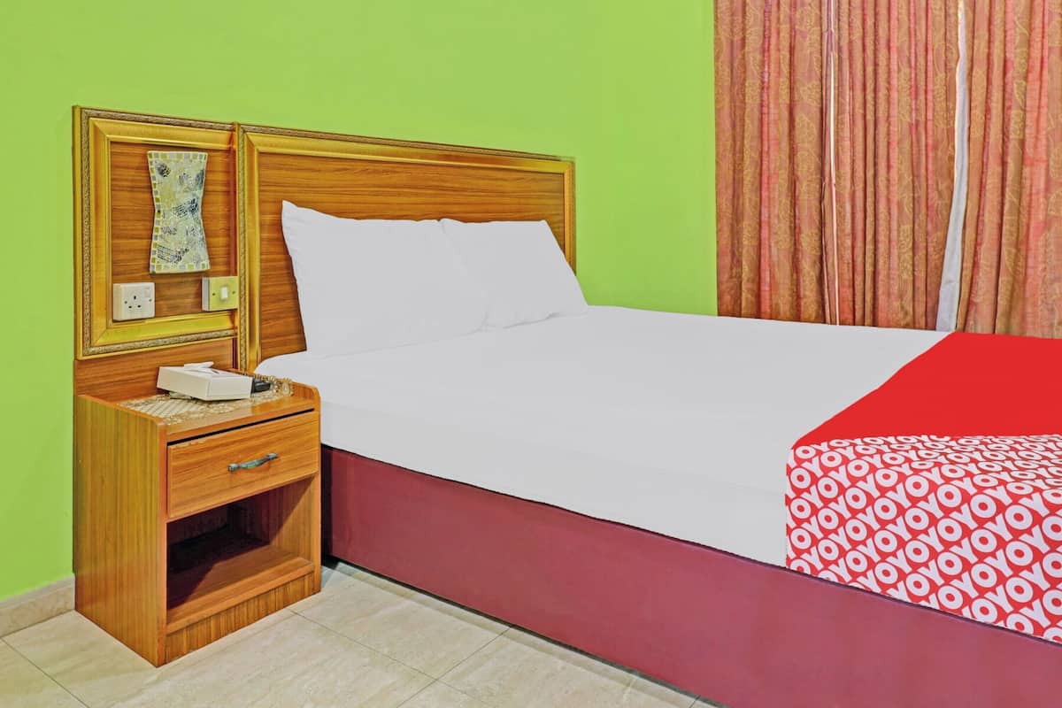 Una cama con ropa de cama blanca, una mesita de noche de madera con un cajón, una mesilla auxiliar y una colcha estampada en rojo y blanco.