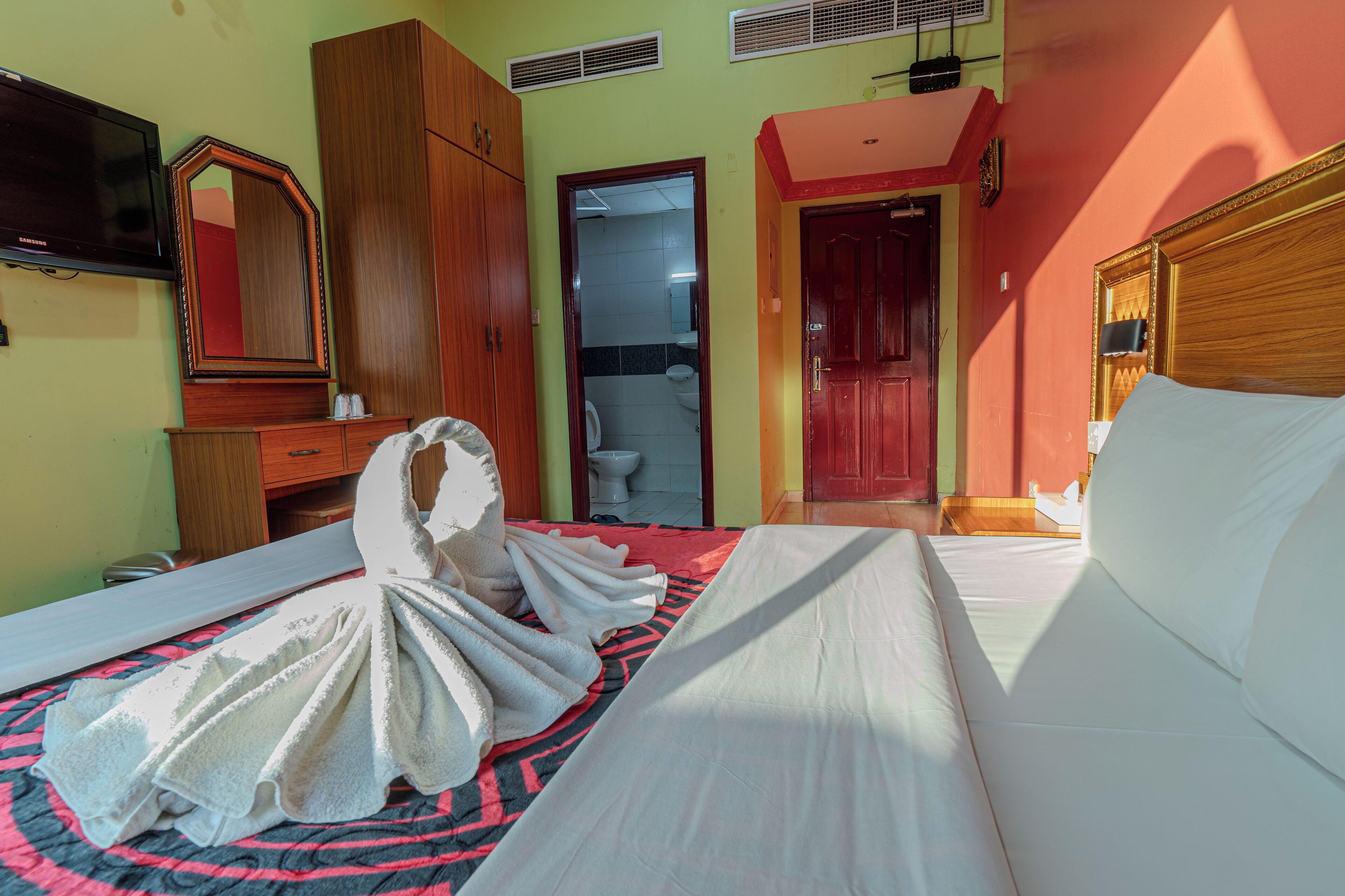 Habitación de hotel con cama, armario de madera, televisor y baño visible a través de una puerta abierta.