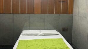 Habitación de hotel con cama, manta verde, paneles de madera y una lámpara sobre la cama.
