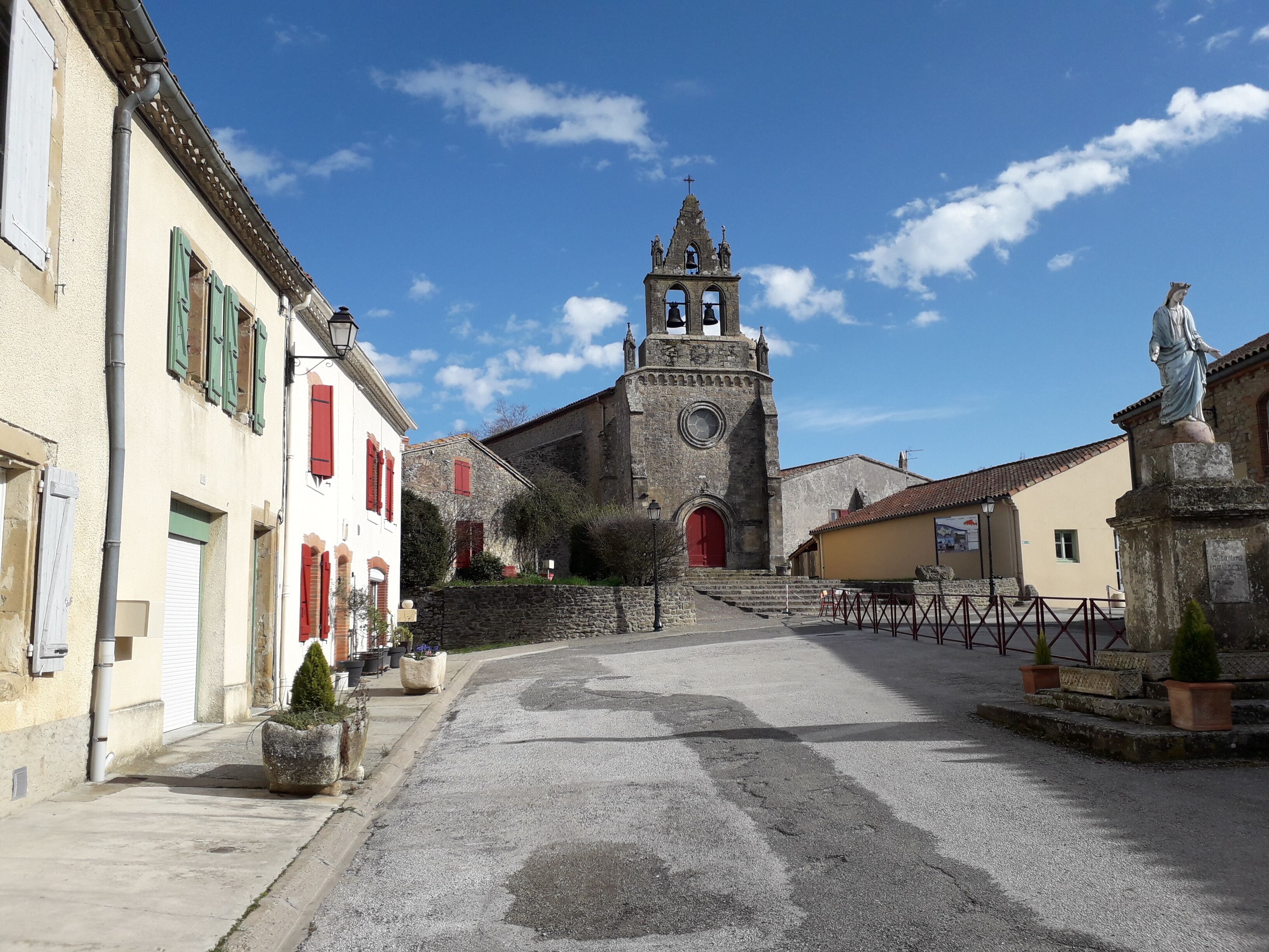 Eine historische Straße mit einer Kirche, die einen Glockenturm und eine Statue zeigt.