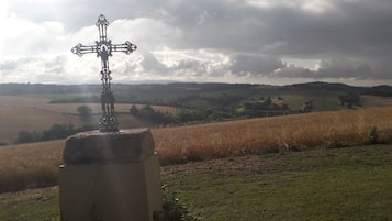 A rural landscape with a cross monument in the foreground and a field in the background.