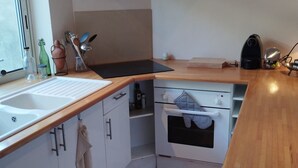 Eine moderne Küche mit weißen Schränken, einer Holz Arbeitsplatte, einem Einbauofen und einem Fenster.