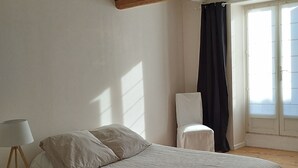 Ein Schlafzimmer mit Bett, Nachttisch, Lampe und einem Fenster mit Vorhängen.