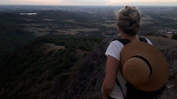 A person with a straw hat and a backpack overlooking a valley with fields and a distant body of water.