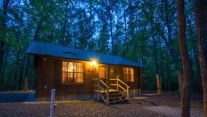 A rustic cabin with a metal roof, wooden exterior, and a gravel driveway. - Julia Cabin is a quaint cabin that sleeps up to 6 people in the existing bedding. (BROKEN BOW)