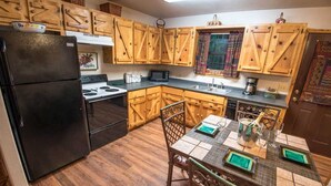 A kitchen with wooden cabinets, a black refrigerator, a stove, a microwave, and a dining table with chairs. - Julia Cabin is a quaint cabin that sleeps up to 6 people in the existing bedding. (BROKEN BOW)