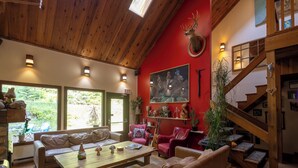 A cozy living room with a red accent wall, a mounted deer head, and a staircase. - Rams Head Inn (Rossland)